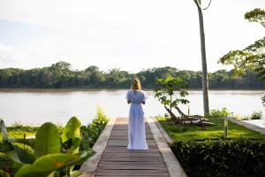 a woman in a white dress standing on a wooden walkway by a lake at Hotel Enai in Puerto Maldonado