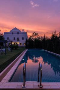 a swimming pool in front of a house with a sunset at Villa Malinee Khao Yai in Ban Tha Chang