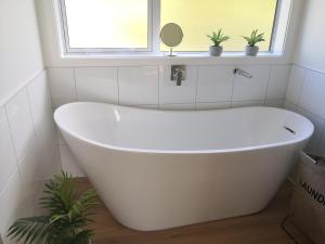 a white bath tub in a bathroom with a window at Karapiro Retreats holiday house in Cambridge