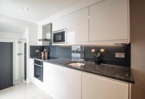 a white kitchen with a sink and a microwave at High Street Kensington by Viridian Apartments in London