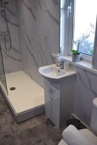 La salle de bains blanche est pourvue d'une douche et d'un lavabo. dans l'établissement Kelpies Serviced Apartments - McClean, à Falkirk