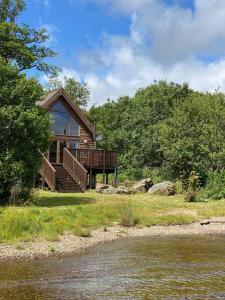 a house with a deck next to a body of water at Lochside Lodge in Dallavich