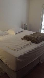 Una cama sin hacer con sábanas blancas y una manta. en Casa beira mar Torres, en Torres