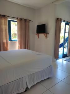 a bedroom with a white bed and a tv at Pousada Vixe Maria in Imbassai