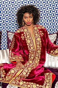 a woman in a red dress sitting on a bed at Riad Fes Nass Zmane in Fès