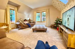eine Frau sitzt auf einer Couch in einem Wohnzimmer mit einem Fernseher in der Unterkunft Ardlinnhe Cottage in Fort William