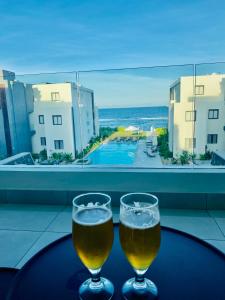 two glasses of beer on a table with a view of the ocean at Eastern Blue Beachfront Luxury Apartment in Poste Lafayette