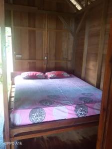 a bed in a wooden room with a pink comforter at Nyang Ebay Surf Camp siberut front E-Bay,Beng-Bengs,Pitstops,Bank Vaults,Nipussi in Masokut