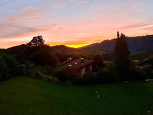 una casa in un campo con un tramonto sullo sfondo di Wunderschöne Wohnung mit Balkon und Blick auf die Alpen a Oberstaufen