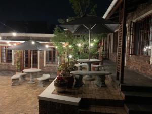 a patio with tables and benches and umbrellas at night at Green Pastures Guesthouse in George
