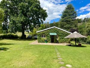 a small building with a grass yard with an umbrella at Esigodini Cottage in Underberg