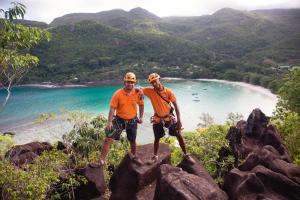 two men standing on rocks in front of a beach at Constance Ephelia in Port Glaud
