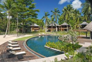 a resort pool with lounge chairs and palm trees at Constance Ephelia in Port Glaud