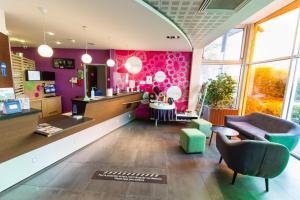 un salón con paredes rosas, un sofá y una silla en ibis Styles Bethune Bruay la Buissière, en Bruay-la-Buissiere