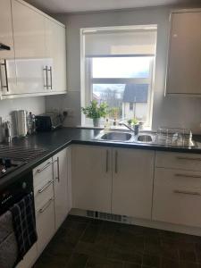 a kitchen with white cabinets and a sink and a window at Two bedroom house in central Portree in Portree