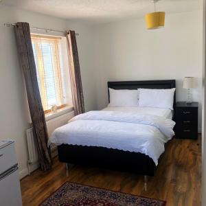 a bedroom with a large bed with white sheets and a window at ASHMINA GUEST HOUSE with Free Onsite Parking in Milton Keynes