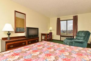 a hotel room with a bed, chair, television and a lamp at Days Inn by Wyndham Ozark Springfield in Ozark