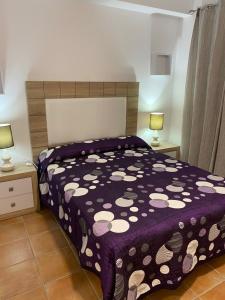 1 dormitorio con 1 cama con edredón morado y 2 lámparas en Precioso apartamento en complejo residencial., en Alcaucín