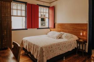 a bedroom with a bed and two windows at Pousada Casa do Pilar in Ouro Preto
