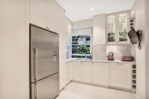 cocina con armarios blancos y nevera de acero inoxidable en Premium Double Bay 3 bedroom apartment en Sídney