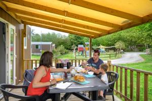 een gezin aan een tafel eten op een veranda bij Camping Capfun La Bretèche in Les Épesses