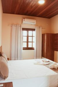 a bedroom with a white bed with a window at Pousada Encantos de Palmeiras in Palmeiras