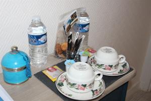 deux tasses et soucoupes sur un comptoir avec bouteilles d'eau dans l'établissement Logis Hôtel & Restaurant Au Clos Paillé Charme & Caractère, à La Roche-Posay