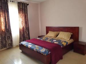 1 dormitorio con 1 cama con cabecero de madera y cortinas en Appartement chic au quartier Omnisport en Yaundé