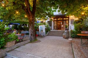 a tree in front of a building with tables and chairs at BIO-Hotel Alter Wirt in Grünwald