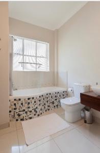 a bathroom with a tub and a toilet and a window at Modern Apartment in Rosebank in Johannesburg