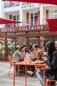 un grupo de personas sentadas en una mesa frente a un hotel en Hôtel Voltaire, en Arles
