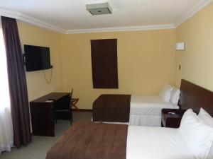 Habitación de hotel con 2 camas, escritorio y TV. en Hotel Costa Pacifico - Express, en Antofagasta