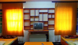 Habitación con 2 camas, cortinas de color naranja y TV. en Hostel Domestika, en Bitola