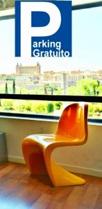 una silla naranja sentada frente a una ventana en TOLETUM low cost LOFTS diáfanos o 2dormitorios PARKING Municipal Gratis al aire libre a 100m en Toledo