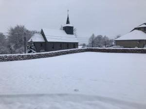 un patio cubierto de nieve con una iglesia al fondo en Residenz Arens en Amblève