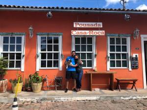 two people standing in front of a red building at Pousada Encanto da Roça in Mucugê