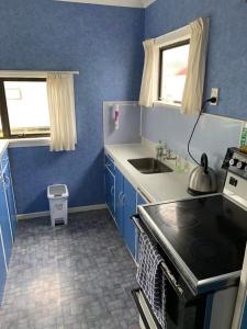 uma cozinha azul com um lavatório e um fogão em Urenui Beach Bach em Urenui