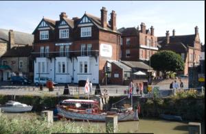 two boats in the water in front of a building at Cosy Sailing Boat Glamping Accommodation on the River in Sandwich in Sandwich