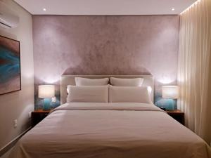 a bedroom with a large white bed with two lamps at Flat Deluxe no centro de Pipa in Pipa