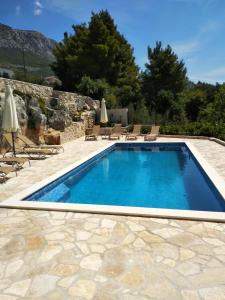 a large swimming pool with a stone wall and chairs at Apartment MareLux in Kaštela