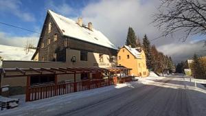 a building on a snow covered road next to a house at Penzion a restaurace V Háji in Loučná pod Klínovcem