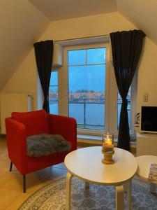 una sala de estar con una silla roja y una mesa con una vela en FeWo Herzstück - Neßmersiel, en Nessmersiel