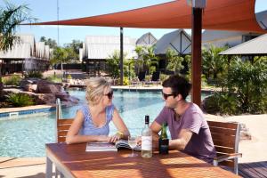 un hombre y una mujer sentados en una mesa cerca de una piscina en Freshwater East Kimberley Apartments, en Kununurra