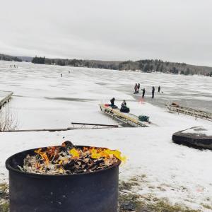 a fire pit on a frozen lake with people on the ice at Baptiste Lake Lodge in Harcourt