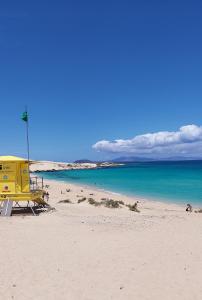 a yellow lifeguard station on a beach with the ocean at Casa Leon Fuerteventura in Corralejo