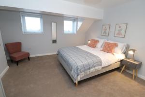 a bedroom with a bed and a chair and two windows at The Snug in Stockton-on-Tees