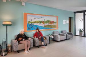 dwoje ludzi siedzących na krzesłach w poczekalni w obiekcie DOMITYS BASALTIK w mieście Agde