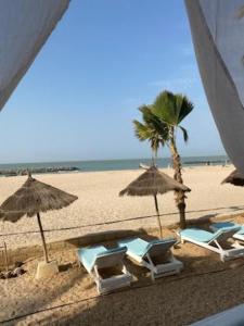 einen Strand mit Liegestühlen und Sonnenschirmen und einer Palme in der Unterkunft West AFRICAN BEACH in Sali Nianiaral