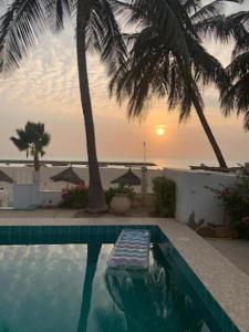 a swimming pool with palm trees and a sunset at West AFRICAN BEACH in Sali Nianiaral