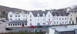 un gran edificio blanco con coches aparcados en un aparcamiento en The Royal Hotel, en Portree